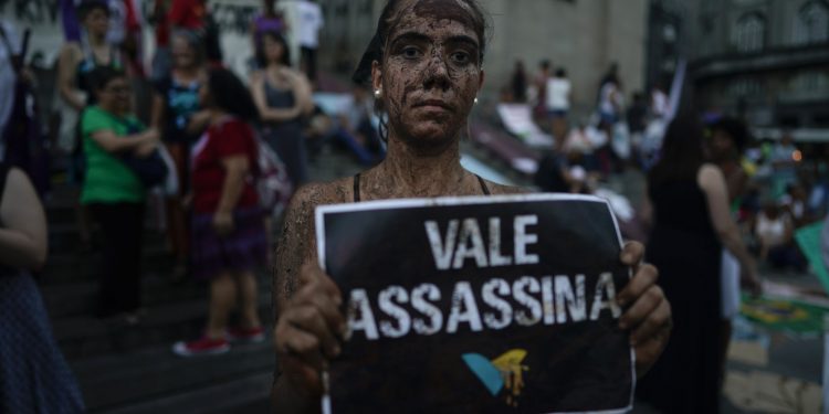 An activists covered in mud poses with a sign that reads "Vale assassin" during a demonstration on the front steps of Sao Paulo's Cathedral, Brazil, Friday, Feb. 1, 2019. (AP)