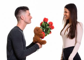 Young happy couple smiling and in love with man giving red roses and teddy bear horizontal shot