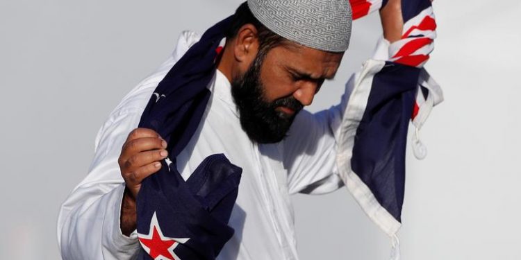 A man holding a New Zealand flag reacts during a burial ceremony for victims of the mosque attacks, at the Memorial Park Cemetery in Christchurch, New Zealand