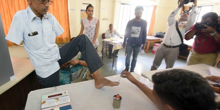 AHMEDABAD, APR 23 (UNI) Polling officials marking a deferently abled voter with indelible ink prior to cast his vote at a polling centre during the 3rd phase of General Election, in Ahmadabad on Tuesday.UNI PHOTO-56U