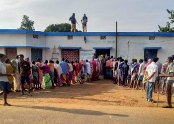 Security personnel stand guard as voters wait in queues to cast their votes during the first phase of Assembly elections in Chhattisgarh at a polling station in Dantewada Monday (PTI photo)