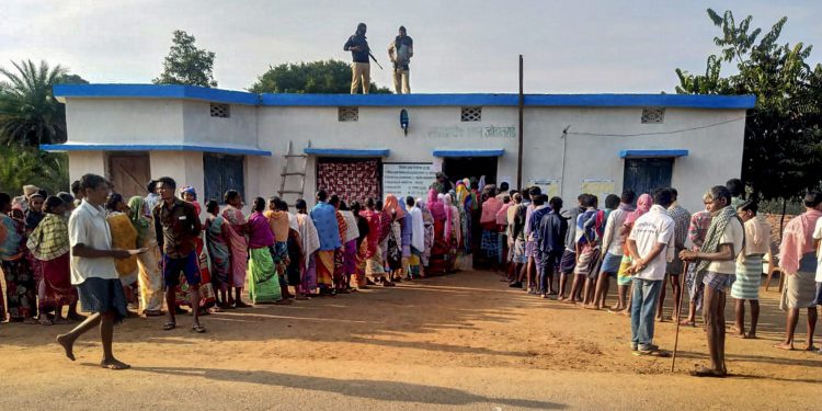 Security personnel stand guard as voters wait in queues to cast their votes during the first phase of Assembly elections in Chhattisgarh at a polling station in Dantewada Monday (PTI photo)