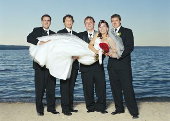 Groom and groomsmen holding bride on beach smiling, portrait