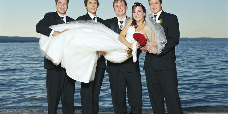 Groom and groomsmen holding bride on beach smiling, portrait