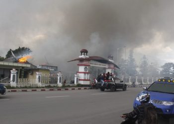 People drive past a blazing government building in Wamena, Monday