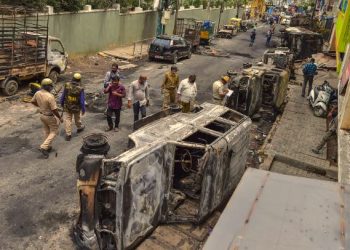 Bengaluru: Police and residents walk past charred remains of vehicles vandalised by a mob over a social media post, allegedly by a relative of a Congress MLA, in Bengaluru, Wednesday, Aug. 12, 2020. (PTI)