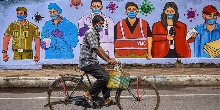 A cyclist rides past a mural paying salute to the frontline corona warriors in Vijayawada, Andhra Pradesh, India. (Image Credit: AFP)