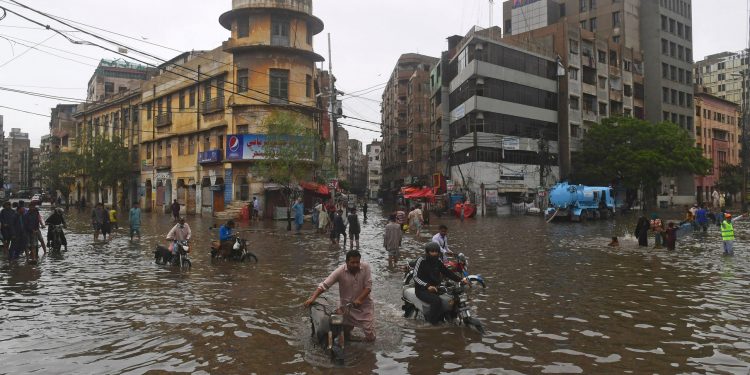 TOPSHOT - People wade across a flooded street after heavy monsoon rainfall in Karachi on July 25, 2022. (Photo by Asif HASSAN / AFP) (Photo by ASIF HASSAN/AFP via Getty Images)